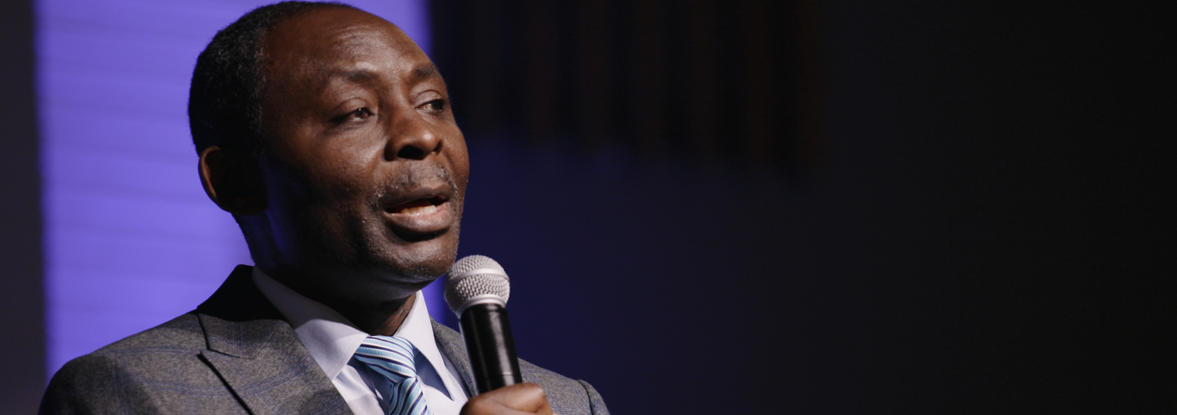 African pastor in gray suit talking into microphone